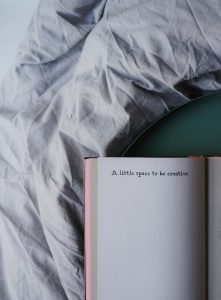 Notebook on a bed with "A little space to be creative" written on it.