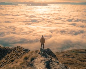 person standing on top pf a mountain overlooking the clouds below