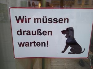 Picture of a sign from a store in Germany: a dog sitting - Wir müssen draußen warten!