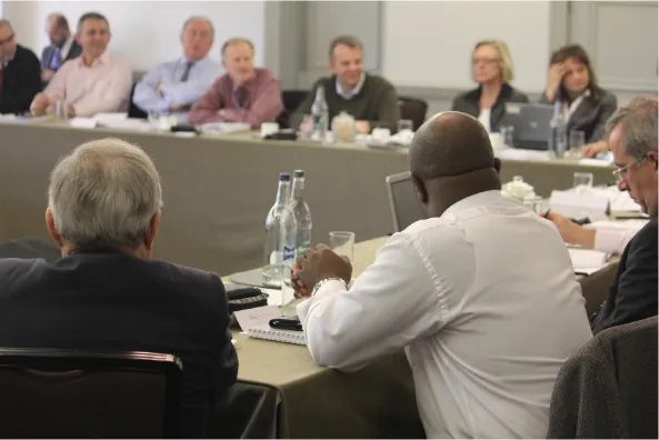 A photograph shows a group of people seated around tables in a meeting room.