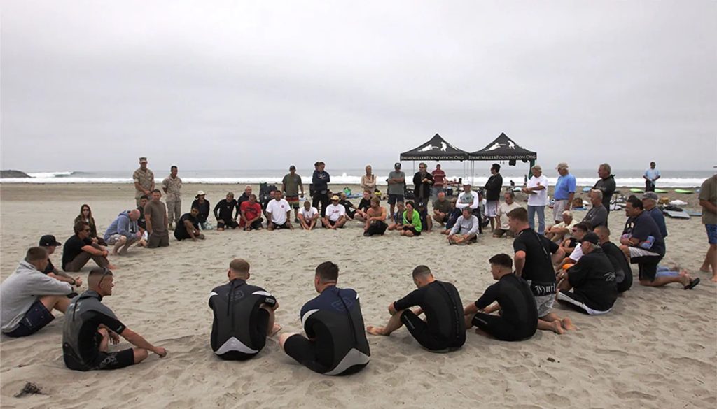 This photo depicts a large group of people sitting in a circle on the beach.