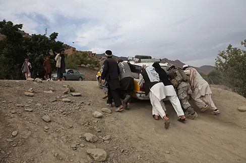 A photograph shows several people pushing a car up an incline.