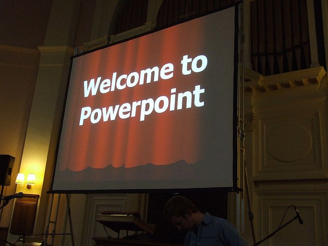 Descriptive image showing a large screen with the words “Welcome to Powerpoint” projected. (11.4.1)