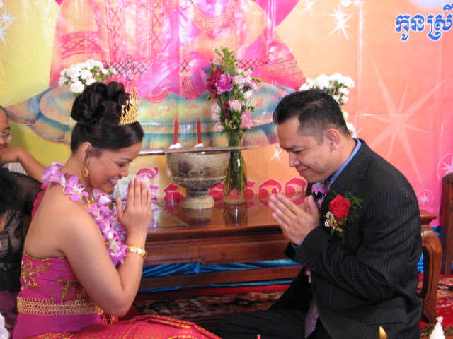 Descriptive image showing a smiling man and woman dressed in formal attire, greeting each other with heads bowed and hands in prayer position. (18.5.0)