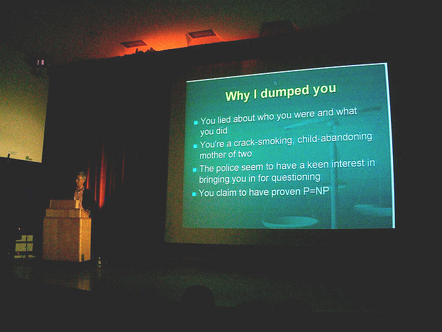 Descriptive image showing a man at a lecturn delivering a presentation. Behind him is a large screen showing a bulleted powerpoint slide titled “Why I dumped you”. (3.4.0)