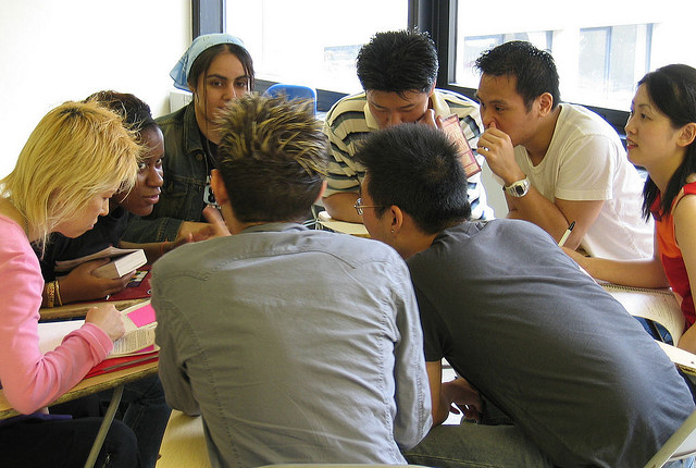 Descriptive image showing a group of diverse people seated at desks, conversing in a close circle. (8.1.1)