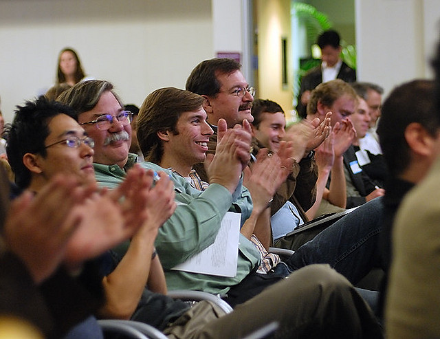Descriptive image showing members of an audience smiling and clapping. (8.2.0)