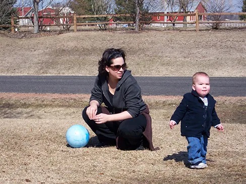 A woman watches a toddler walk away from her.