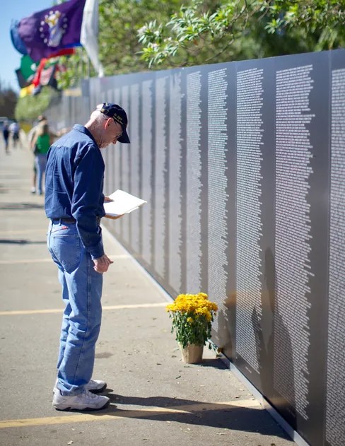 A photograph shows a person looking at the Vietnam Traveling Memorial Wall in the United States.