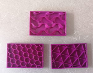 A photo of three 3D printed models, showing three different styles of infill patterning. The first model has a wavy gyroid pattern. The second model has a hexagonal pattern. The third model has a triangular pattern