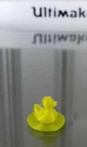 A picture of a small 3D printed duck sitting on top of a bed of layered filament.